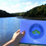 Le Léguer, fleuve des Côtes d'Armor en Bretagne, est labellisé "Sites Rivières Sauvages" depuis le 20 octobre 2017. Le logo bleu du label devant le fleuve Léguer, sous le ciel bleu.